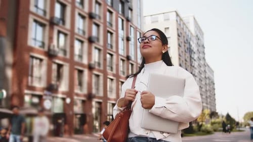 Young Professional Woman Holding Laptop and Looking Up in the City