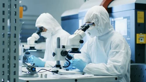 Deux ingénieurs/scientifiques/techniciens vêtus de combinaisons stériles pour salles blanches utilisent des microscopes pour le composant Adj