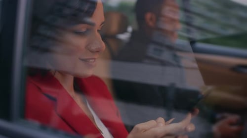 Young Woman and Man Riding on the Backseat of a Car in the Evening. They Both Use Smartphones, Brow