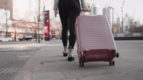 Woman Walking on a City Street and Rolling a Wheeled Suitcase Behind Her Close Up View From Behind