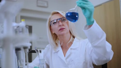 Female Scientist Examines Blue Liquid in Laboratory Beaker