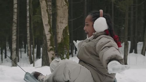 Eltern ziehen verspieltes Mädchen auf Schneeschlitten durch den Winterwald