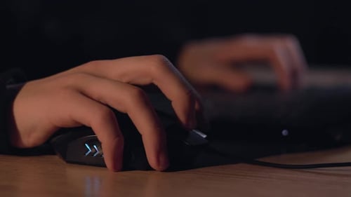 Gros plan des mains d'un joueur utilisant une souris d'ordinateur jouant à un jeu vidéo la nuit. Un hacker masculin fait une pause