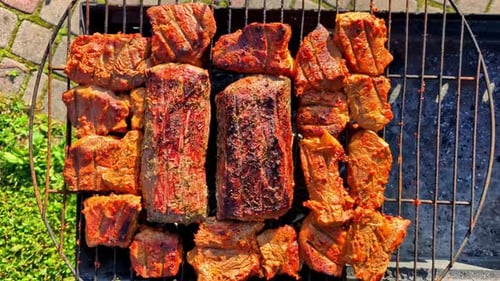 Large ribs and steaks sizzle on the grill, surrounded by smoky chops and kabobs