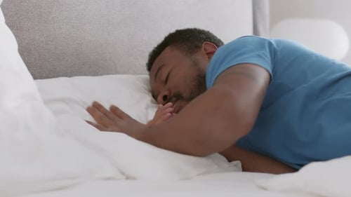 Nahaufnahme eines jungen afroamerikanischen Mannes, der auf dem Bett liegt und es sich bequem macht zu schlafen