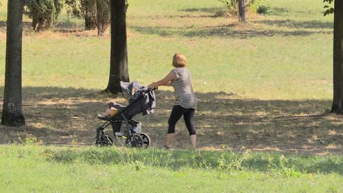 Mother Walking with Her Son Who is Sleeping in a Stroller in Autumn Park Raising Children Recreation