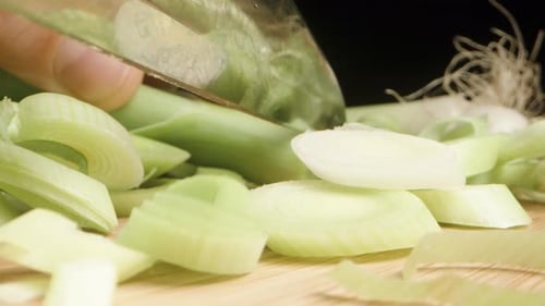 I am slicing green leek on a wooden cutting board with a black background, macro shot.