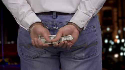 Close Up Mans Hands in Handcuffs Holding Dollar Banknotes