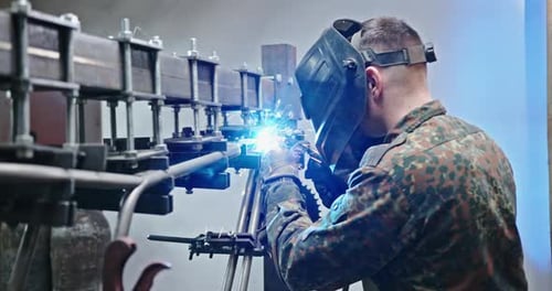 Mann schweißt Metallkonstruktion in der Werkstatt, Seitenansicht eines männlichen Arbeiters beim Absenken des Schutzschildes und