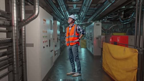 Full Body Side View Of Asian Male Engineer Looking Around With Arms Akimbo In Engine Control Room