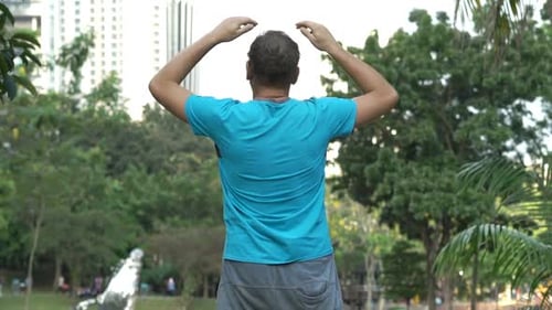 Attractive young man stretching arms after jogging workout in city park