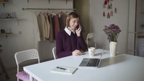 Woman Using Phone and Laptop at White Desk
