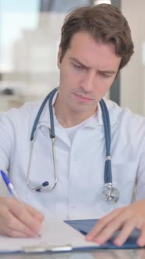 Focused Doctor Writing on Clipboard in Medical Office