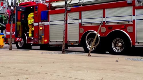 1-2Red Fire Truck parked in a downtown city next to a yellow fire hydrant with blue caps and firefig