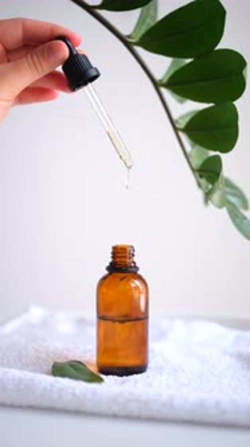 Glass cosmetic bottle with oil. Oily drop falls from cosmetic pipette.