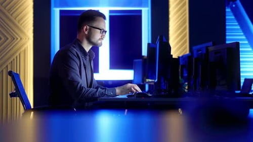 Mann arbeitet am Laptop im Serverraum mit leuchtenden Datenracks und blauen Techniklichtern.