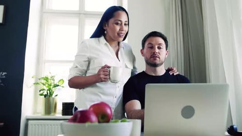 Couple smiles looking at laptop in bright modern home
