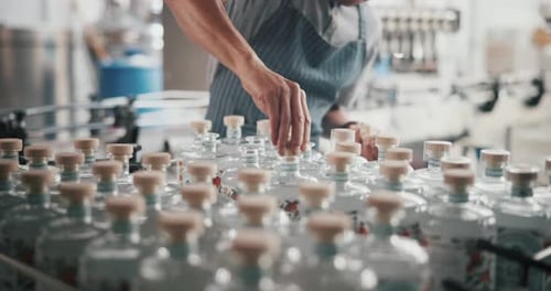 Hands, man and packaging alcohol at distillery with gin bottles for manufacturing