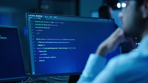 Fokussierter Softwareentwickler, der komplexen Code auf einem Computerbildschirm in einem dunklen Hightech-Büro eingibt.
