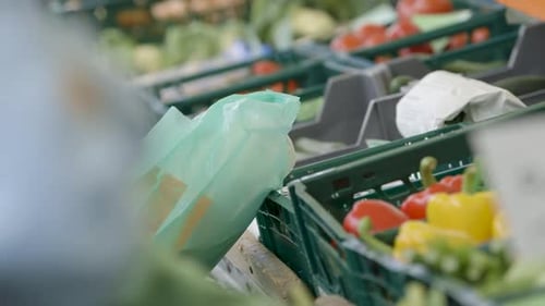 Primer plano de una bolsa de plástico con alimentos, coloridas verduras frescas de fondo en un mercado