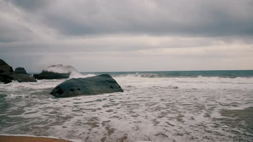 Slow motion water splashing on the rocks in a seashore on a cloudy day with blue sea