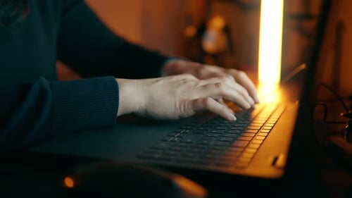 Woman Typing on Laptop in Warmly Lit Room
