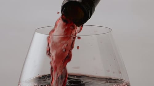 Gourmet-Rotweinstrahl, der aus der Flasche in den transparenten Kelch gegossen wird, Nahaufnahme