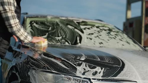 Man Cleaning Car Hood with Sponge at Outdoor Car Wash