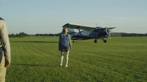 Woman and Man Walk Toward Biplane on Airfield