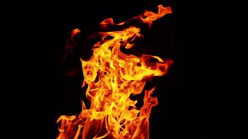 Beautiful fire flames moving in the darkness. Multiple sparks fly up and smoke rises behind.