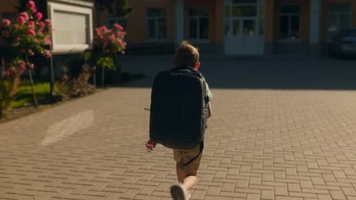 Excited Schoolboy with Backpack Running Toward School on a Sunny Day