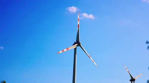 Windmill blades rotating slowly. Low angle view at the wind turbine at the backdrop of blue sky.