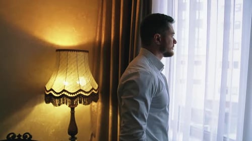Hübscher Mann nach der Arbeit in der Wohnung. Junger Geschäftsmann am Fenster im dunklen Hotelzimmer.