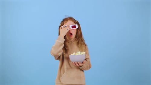 Child Wearing 3D Glasses Holding a Bowl of Popcorn in Front of a Blue Background During a Fun Movie