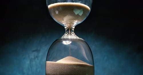 Concept of turning back time. Hourglass with grains of sand on a dark background. Shot on super slow