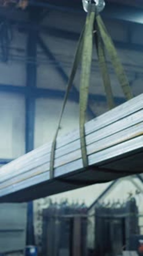 Factory Worker Lifts Heavy Metal Beams in Industrial Workspace
