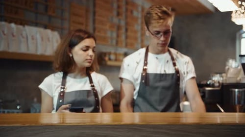 Two employees stands in the cafe. Guy putting cup with cofee on the table