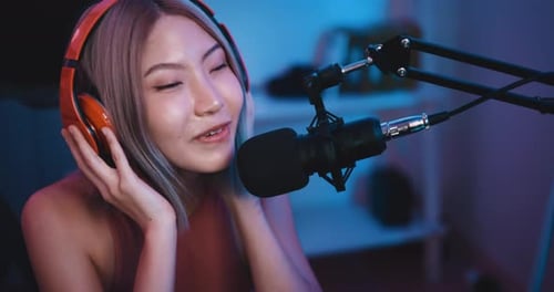 Jeune influenceuse asiatique portant des écouteurs parlant dans un microphone tout en enregistrant une radio