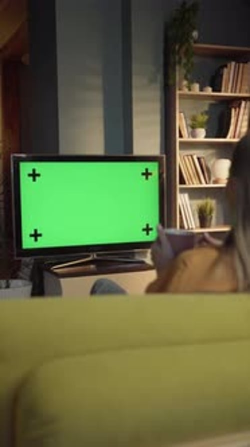 Woman Relaxing on a Sofa in a Cozy Living Room Watching a Television with a Green Screen Display