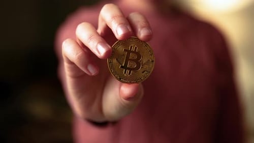 Main de femme montrant une pièce d'or bitcoin à la caméra