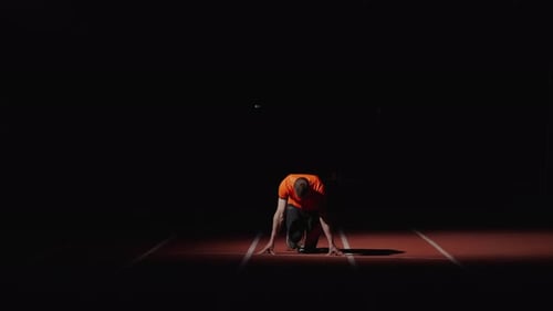 Professional Sprinter Runner Starting From Low Start Position In Dark Stadium Frontal View