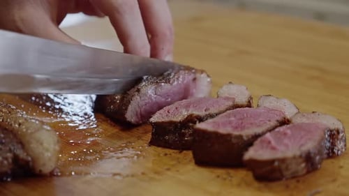 Chopping Juicy Fried Steak with Steel Knife on Wooden Board – Detailed View