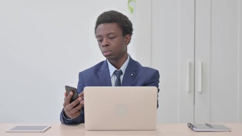 Young Adult Using Phone at Desk With Laptop