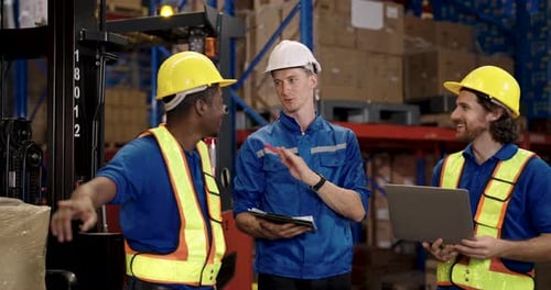 Warehouse workers of different ethnicities discuss shipping logistics while checking clipboard and