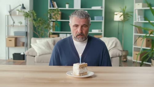 A Sad Elderly Man Celebrates the Holiday Alone Blowing Out a Candle on a Cake