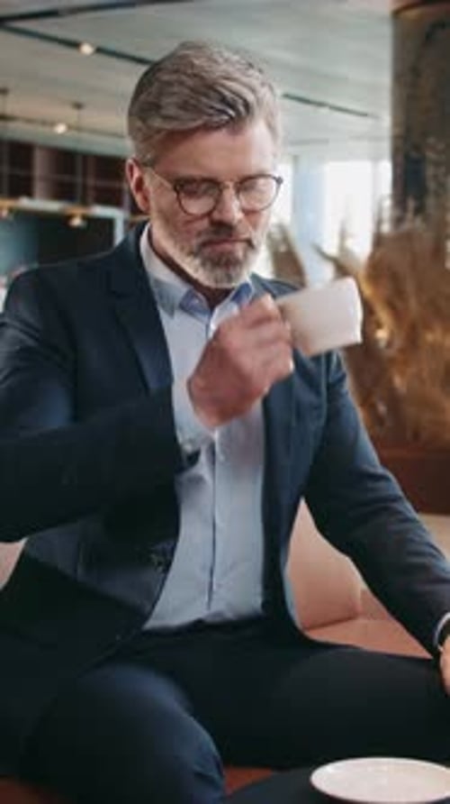 Welldressed Businessman Sitting at Table in Cafe Drinking Coffee Looking at Watch Shot of