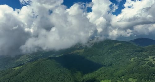 Flying trough white fluffy clouds above green mountain peaks. Beautiful summer sunny day on the high