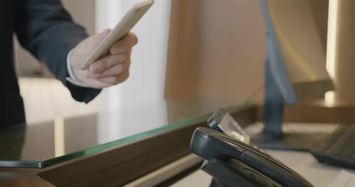 Closeup of Male Hand Making Electronic Payment with Smartphone at Reception Desk in Hotel