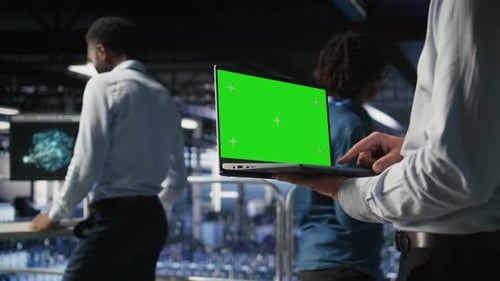 Nahaufnahme eines Mitarbeiters im Serverraum, der einen Greenscreen-Laptop neben einem Kollegen verwendet