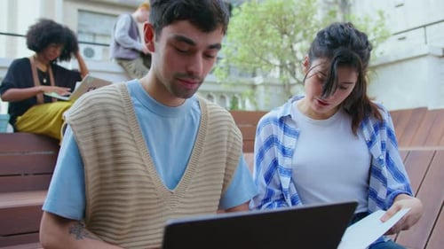 Young Coworkers Using Laptop and Discussing Notes Outdoors in the City